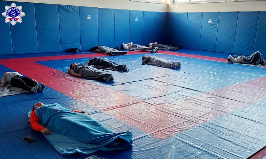 Słuchacze szkolenia zawodowe podstawowego podczas treningu antystresowego, leżący na matach w hali sportowej Szkoły Policji w Pile, przykryci kocami