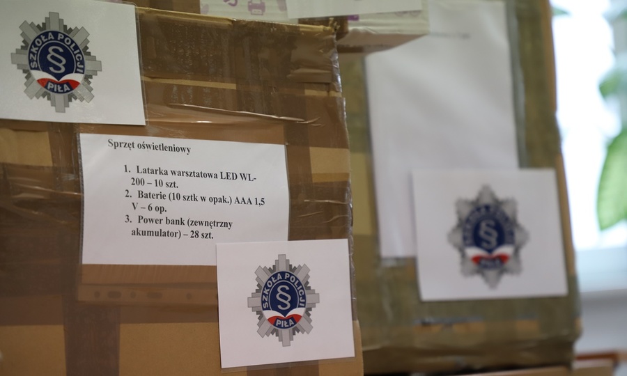 Kartonowe pudełka z logo Szkoły Policji w Pile z zawartością darów zebranych dla Ukrainy.