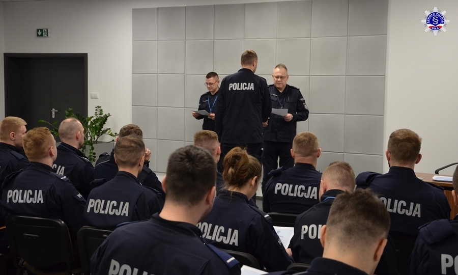 Aula akademika Szkoły wypełniona umundurowanymi policjantami podczas uroczystego zakończenia kursu specjalistycznego doskonalącego wiedzę i umiejętności absolwentów szkolenia zawodowego podstawowego realizowanego w warunkach ogłoszonego stanu zagrożenia epidemicznego lub stanu epidemii