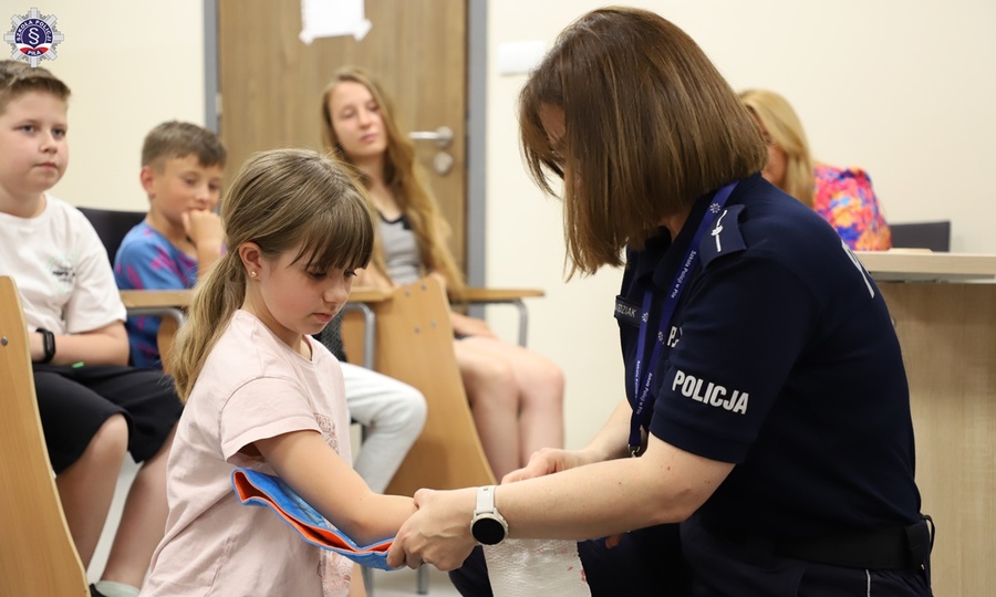 Policjantka w mundurze zakłada dziewczynce usztywnienie kończyny górnej.