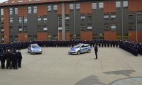 Umundurowani policjanci stojący w szyku na placu apelowym. Na środku placu stoją dwa oznakowane radiowozy.