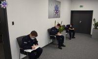 Trzech umundurowanych funkcjonariuszy siedzi na krzesłach i wypełnia formularze zgłoszeniowe.