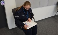 Umundurowana policjantka siedzi na krześle i wypełnia formularz zgłoszeniowy.
