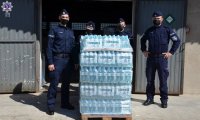 Słuchacze Szkoły Policji w Pile w maseczkach na twarzy stoją przy palecie z wodą butelkowaną.