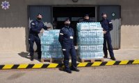 Słuchacze Szkoły Policji w maseczkach na twarzy przed halą magazynową. Obok nich dwie palety wody butelkowanej.