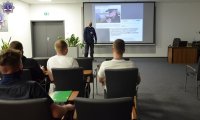 Umundurowany policjant prowadzi wykład dla słuchaczy.