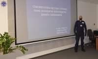 Umundurowany policjant prowadzi wykład, w tle wyświetlana prezentacja multimedialna