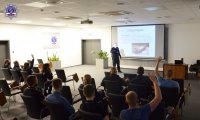 Nauczyciel policyjny podczas podczas wykładu na auli akademika Szkoły Policji w Pile.  W tle prezentacja multimedialna dot. kolizji drogowej.
