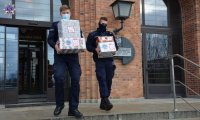 Dwóch umundurowanych policjantów schodzi po schodach niosąc przygotowane paczki.