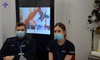 Dwóch policjantów w maseczkach, w tle widać pokaz multimedialny.