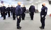 Umundurowany policjant składa meldunek Zastępcy Komendanta Szkoły Policji w Pile. W tle stoją umundurowani policjanci i policjantki.