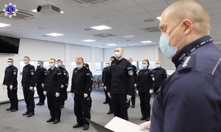 Umundurowani policjantki i policjanci w maseczkach na twarzy stoją w auli akademika.