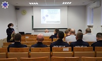 Kobiety i mężczyźni słuchający wykładu umundurowanej policjantki. Na ekranie wyświetlana prezentacja multimedialna.