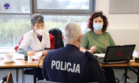 Dwie Panie z personelu medycznego siedzące na krześle przeprowadzają wywiad medyczny z policjantem.