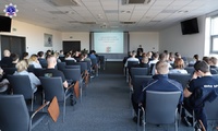 Kobiety i mężczyźni słuchający wykładu umundurowanej policjantki. Na ekranie wyświetlana prezentacja multimedialna.