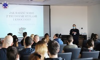 Kobiety i mężczyźni słuchający wykładu umundurowanej policjantki. Na ekranie wyświetlana prezentacja multimedialna.