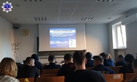 Grupa osób słuchająca wykładu. W tle ekran z wyświetlaną prezentacją multimedialną.