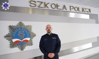 Umundurowany policjant stoi na tle logo Szkoły Policji w Pile.