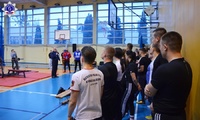 Grupa osób uczestniczących w zawodach w wyciskaniu sztangi  na sali gimnastycznej  podczas przemówienia Zastępcy Komendanta Szkoły Policji w Pile.