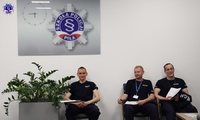 Trzech umundurowanych policjantów siedzi na krzesłach w sali.