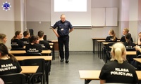 Uczniowie klas policyjnych siedzący w ławkach podczas zajęć z umundurowanym funkcjonariuszem
