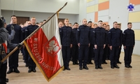Sztandar Szkoły Policji w Pile. W tle stoją słuchacze w umundurowaniu ćwiczebnym.
