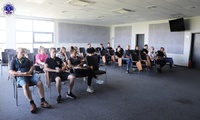 Grupa osób, kobiety i mężczyźni siedzący na sali wykładowej w trakcie zajęć.