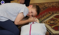 Dziecko ćwiczy zasady udzielania pierwszej pomocy na manekinie i symuluje sprawdzenie oddechu u poszkodowanego