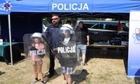 Nauczyciel policyjny, a obok niego dwójka dzieci, w rękach trzymają tarcze z napisem policja.