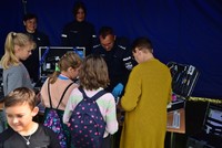 Dzieci stojące przy stoisku – niebieskim namiocie technika kryminalistyki Szkoły Policji w Pile ramach VI Rajdu Granicznego Nordic Walking w Jeziorkach.