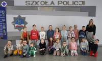 Pamiątkowe zdjęcie dzieci wraz z opiekunką przy tablicy z logo Szkoły Policji w Pile