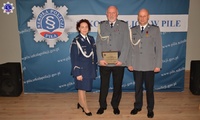 Na środku stoją trzy osoby, Komendant Szkoły Policji w Pile ze swoim Zastępcą oraz wyróżniony funkcjonariusz, w tle baner z logo Szkoły Policji w Pile