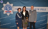 Na środku stoją trzy osoby, Komendant Szkoły Policji w Pile ze swoim Zastępcą oraz wyróżniony pracownik, w tle baner z logo Szkoły Policji w Pile