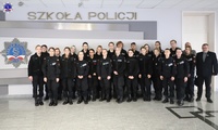 Zdjęcie grupowe umundurowanych uczniów klas policyjnych stojących na holu. W tle logo Szkoły Policji w Pile.