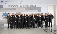 Zdjęcie grupowe umundurowanych uczniów klas policyjnych stojących na holu. W tle logo Szkoły Policji w Pile.