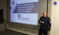 Umundurowany policjant w trakcie wykładu. W tle ekran na którym wyświetlony jest napis Kształtowanie się międzynarodowego systemu ochrony praw człowieka.