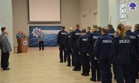 Słuchacze Szkoły Policji stoją w umundurowaniu ćwiczebnym. Przy mównicy umundurowany policjant przemawia do zgromadzonych.