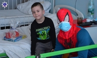 Mały chłopiec siedzi na szpitalnym łóżku w towarzystwie spidermana. Na łóżku prezent, który otrzymał od przedstawicieli szkolnego samorządu.