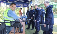 Policjanci patrzą na drona przy niebieskim namocie.