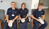 Umundurowana słuchaczka i dwóch słuchaczy słuchaczy Szkoły Policji w Pile siedzący na krzesłach i trzymający w ręku dokumentację do pobrania krwi
