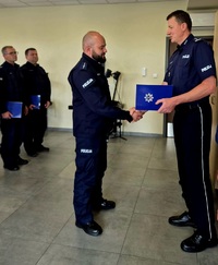 Zdjęcie kolorowe, policjanci w niebieskich mundurach kończący kurs dla techników kryminalistyki. Zastępca Komendanta Szkoły wręcza świadectwa ukończenia kursu w obecności kadry dydaktycznej Szkoły