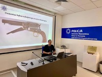 wykładowca podczas zajęć, w tle prezentacja broni czarnoprochowej.