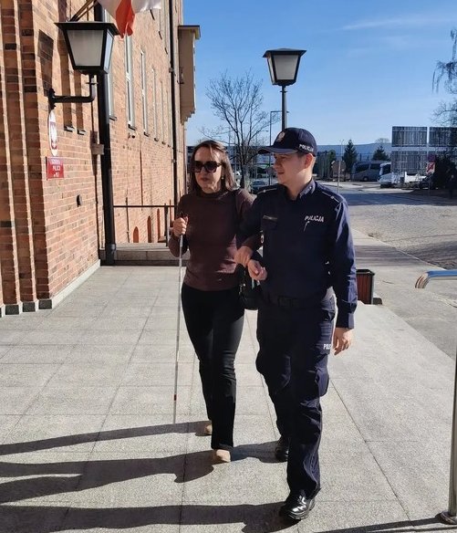 policjantka prowadzi osobę niewidomą przy wejściu do budynku Szkoły Policji w Pile