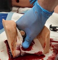 Zbliżenie na trenażer "szyja" masywnego krwotoku, policjant w nylonowych rękawiczkach powstrzymuje krwawienie.