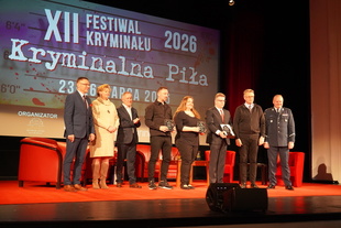 Laureaci oraz gospodarze Festiwalu stoją na scenie z nagrodami i  uśmiechają się do wspólnego zdjęcia.