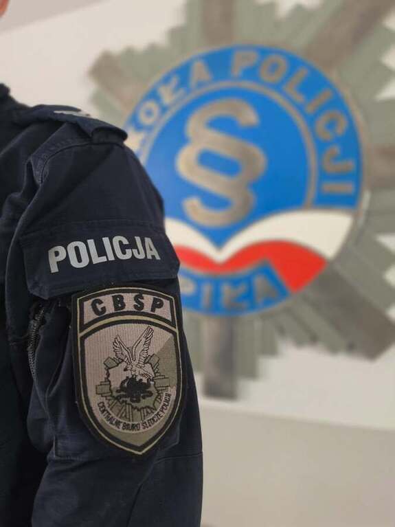 naszywka CBŚP na lewym ramieniu, w tle szyld Szkoły Policji w Pile